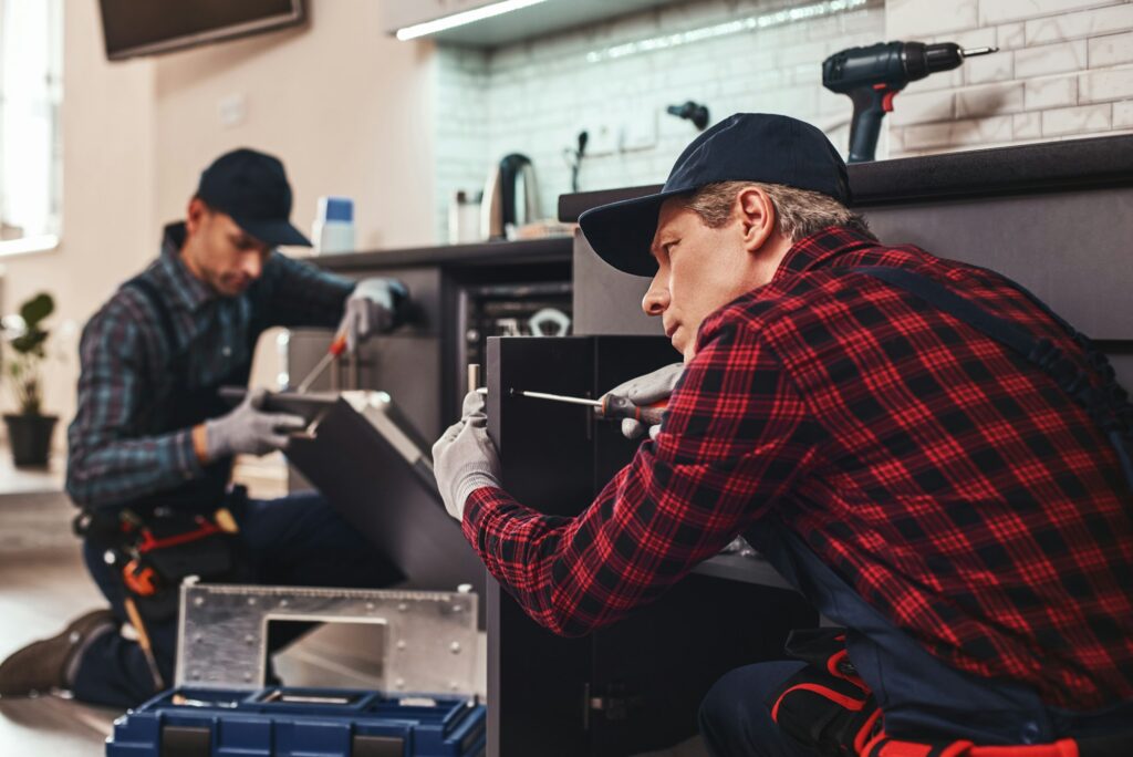 Quick and quality repairment. Two men technician sitting near dishwasher